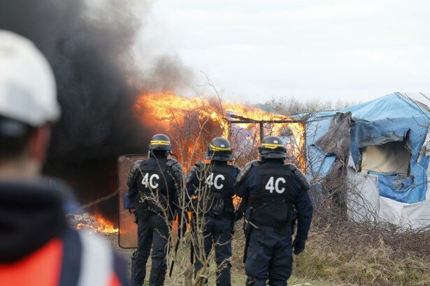 French CRS riot police watch as smoke and flames billow from a burning makeshift shelter during a protest by migrants against the partial dismantlement of the camp for migrants called the "jungle", in Calais